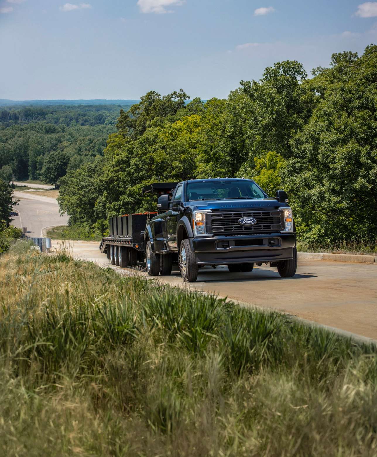 Black Ford Super Duty towing a loaded flatbed trailer up a wooded hill road, diesel work near Farmington MO