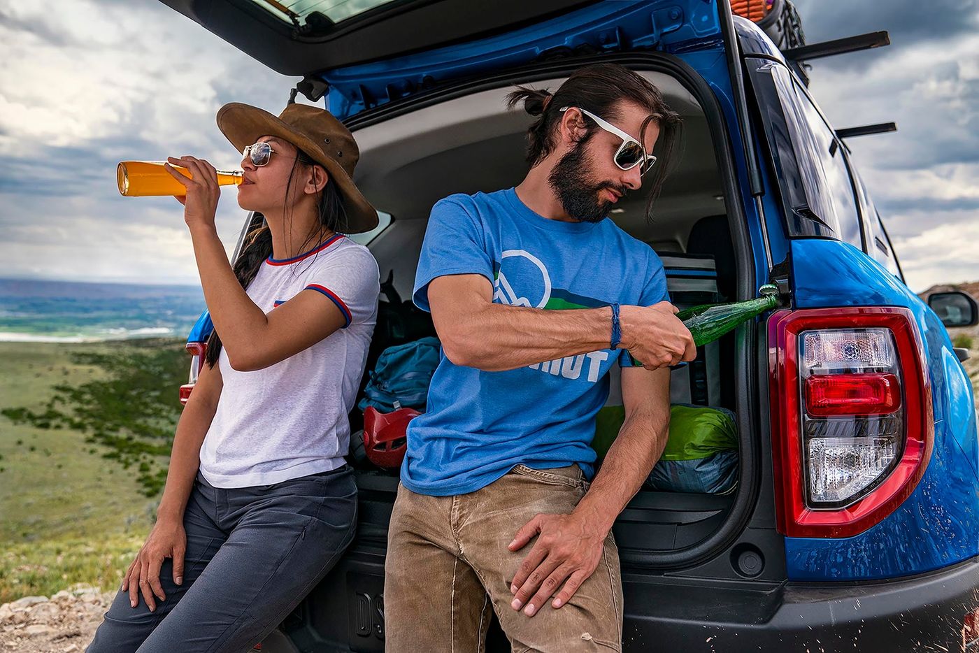 Couple relaxing at the open liftgate of a blue Ford Bronco Sport loaded with camping gear, Farmington MO