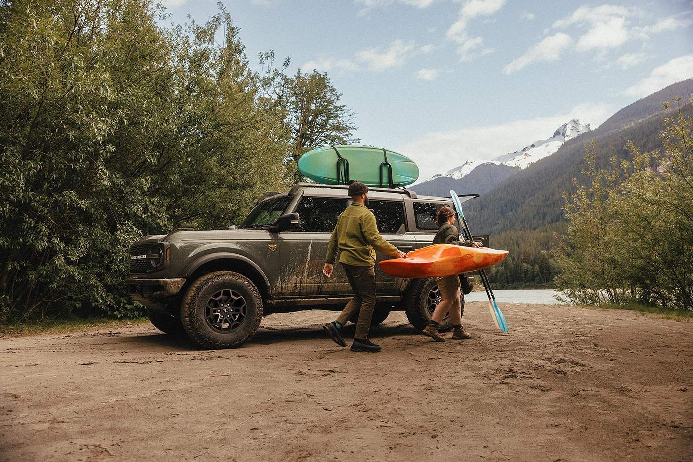 Couple carrying a kayak from a Ford Bronco parked at a mountain lake, a weekend SUV for Farmington MO buyers
