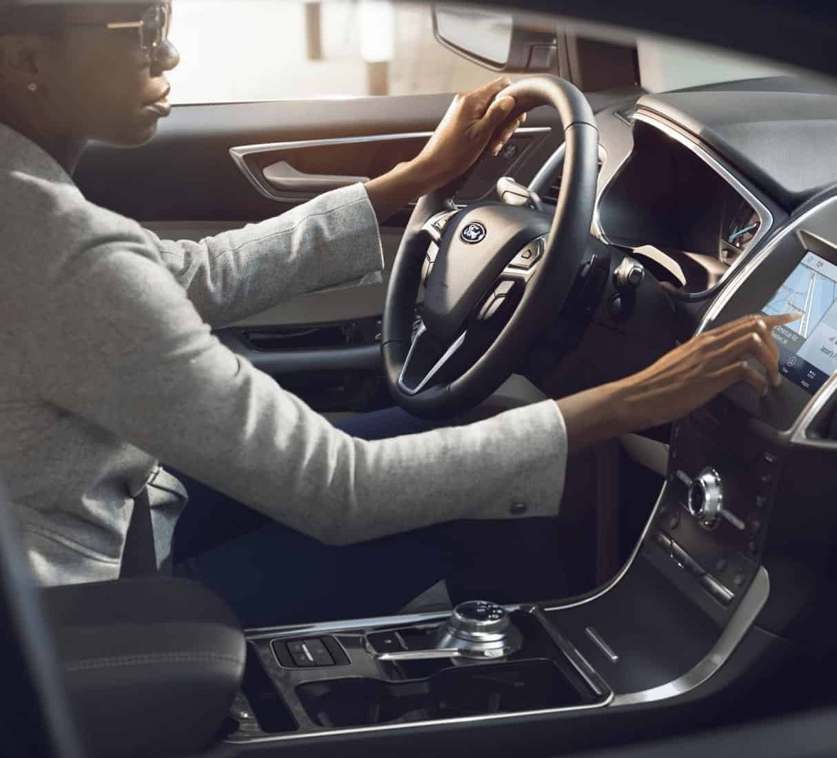 Driver reaching over to tap the center touchscreen in a Ford interior, commuter tech for Farmington MO