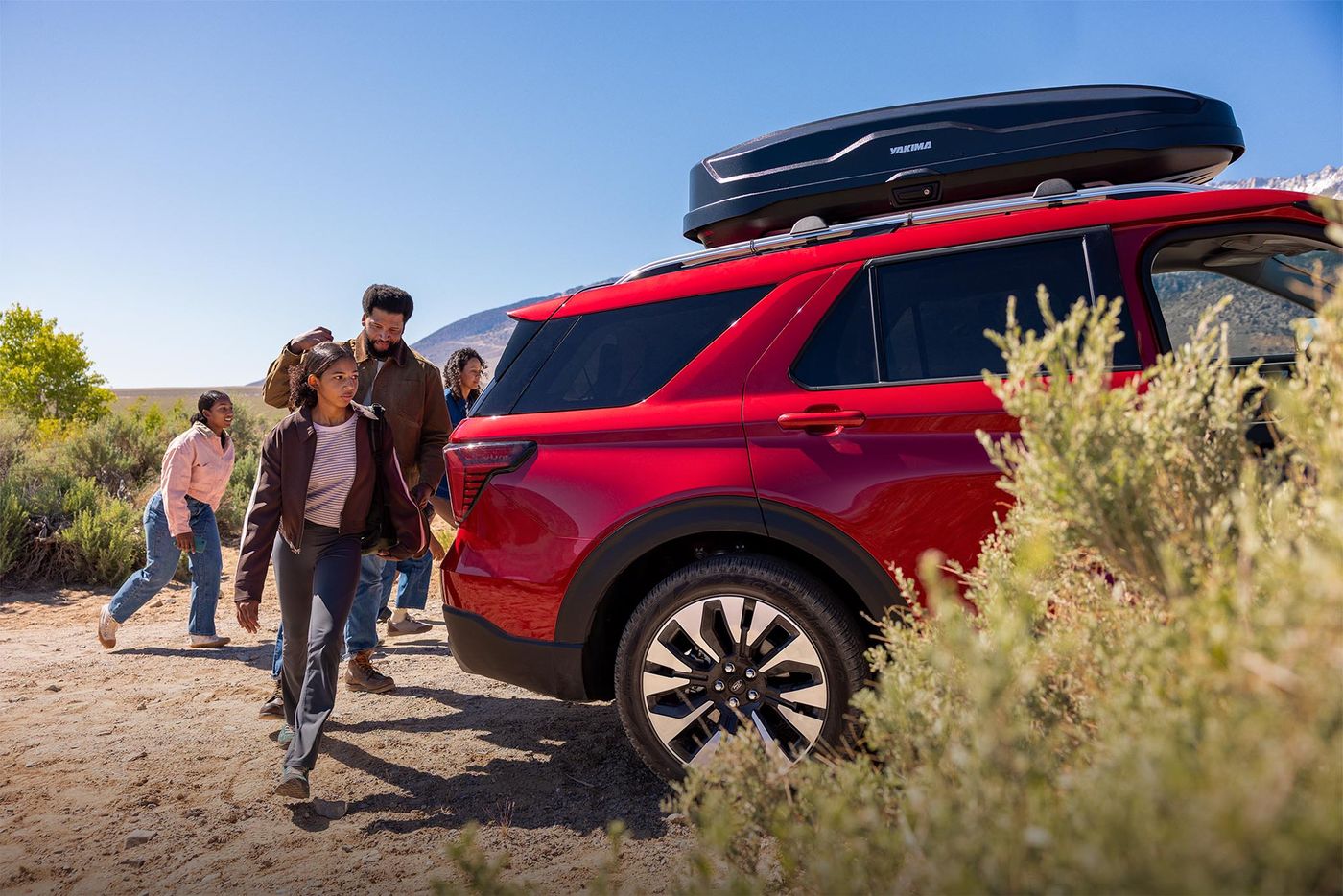 Family walking around the back of a red Ford Explorer on a desert trail, family SUV shopping in Farmington MO