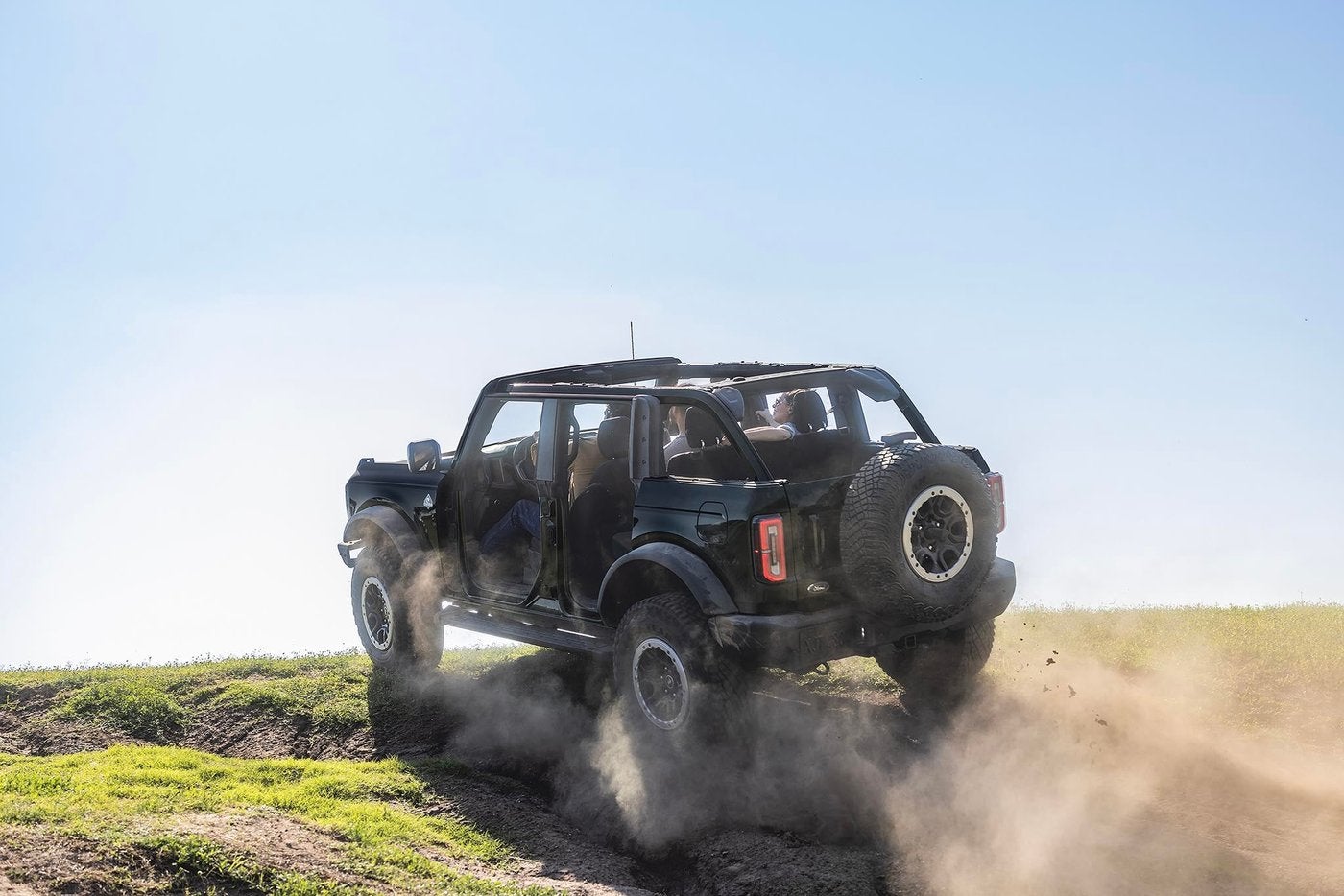 Black four door Ford Bronco with the doors and roof off kicking up dust on a grassy hill, Farmington MO