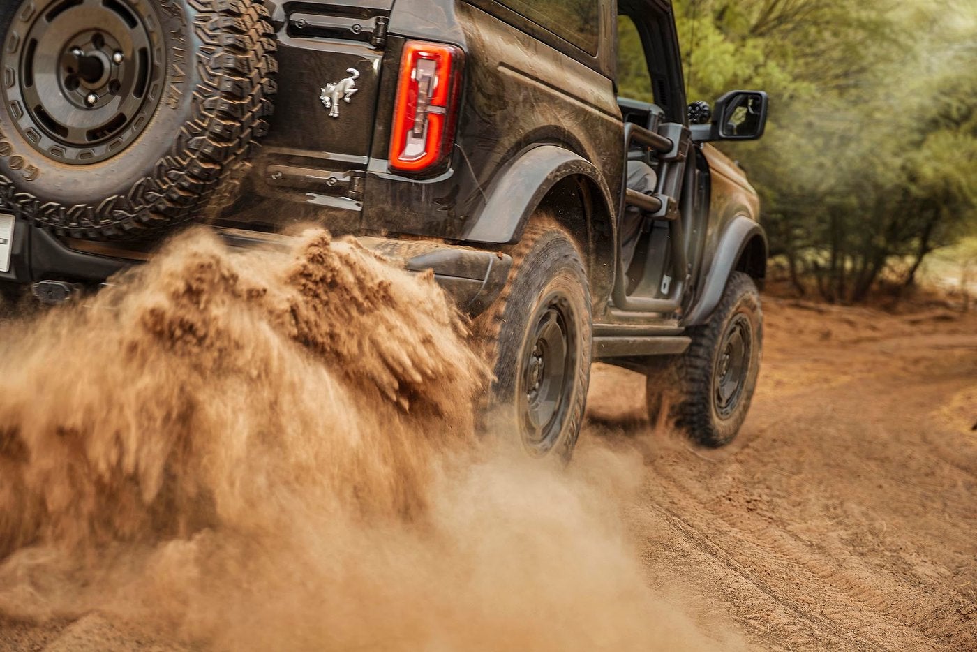 Ford Bronco kicking up dirt on a wooded trail with its spare tire in view, trail driving near Farmington MO