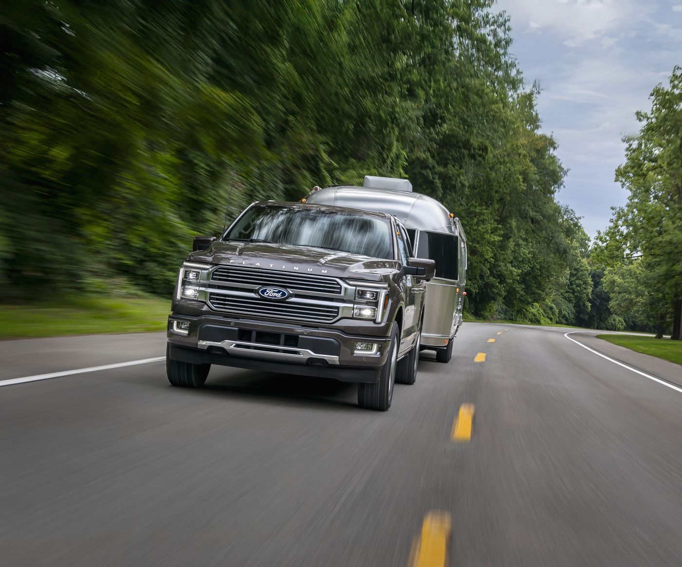 Gray Ford F-150 Platinum pulling a silver camper down a tree lined road, towing season in Farmington MO