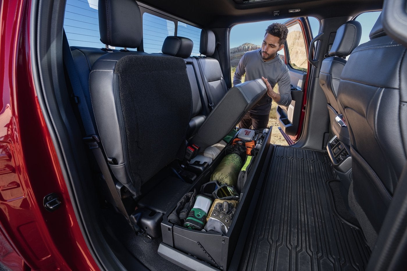 Man lifting the rear seat of a red Ford F-150 to reach the lockable storage bin, Farmington MO