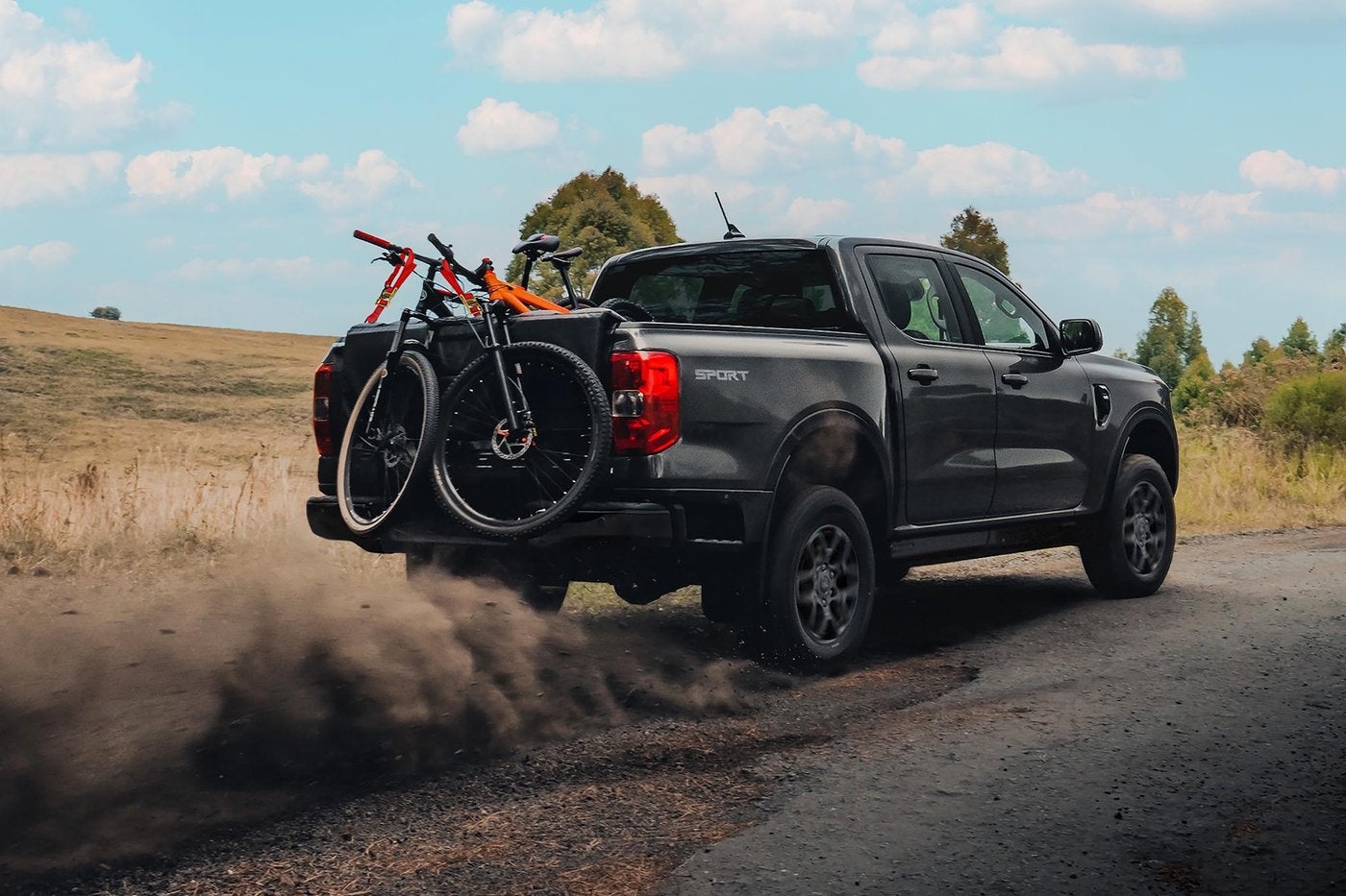 Dark gray Ford Ranger with bikes on the tailgate kicking up dust on a gravel road, Farmington MO