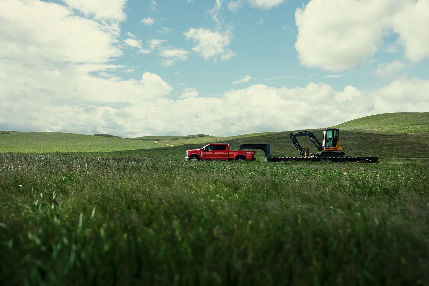 Red Ford Super Duty F-250 Lariat towing a gooseneck trailer with a mini excavator across a green field, Farmington MO