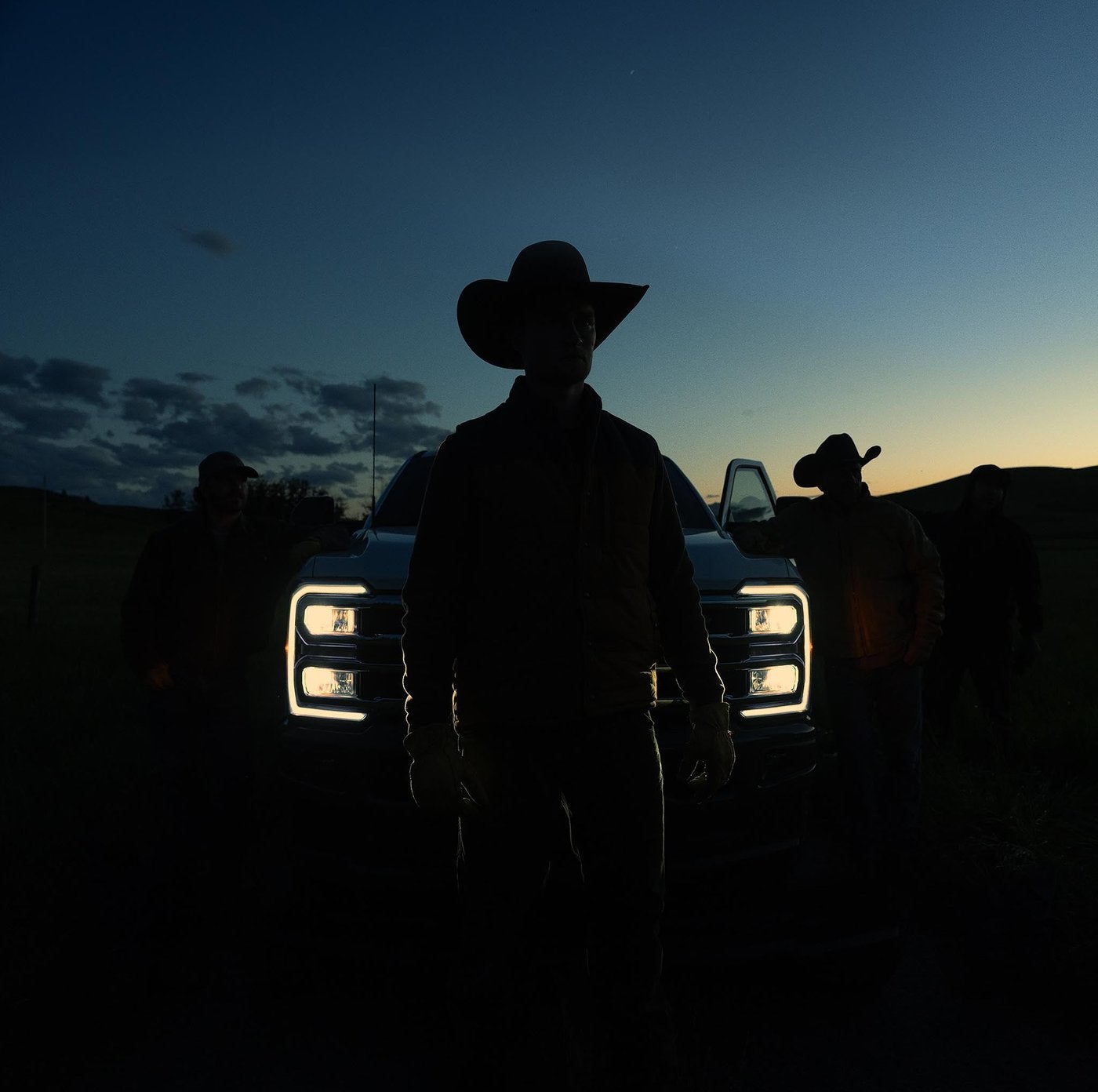 Rancher in a cowboy hat silhouetted in front of a Ford Super Duty with headlights on at dusk, Farmington MO