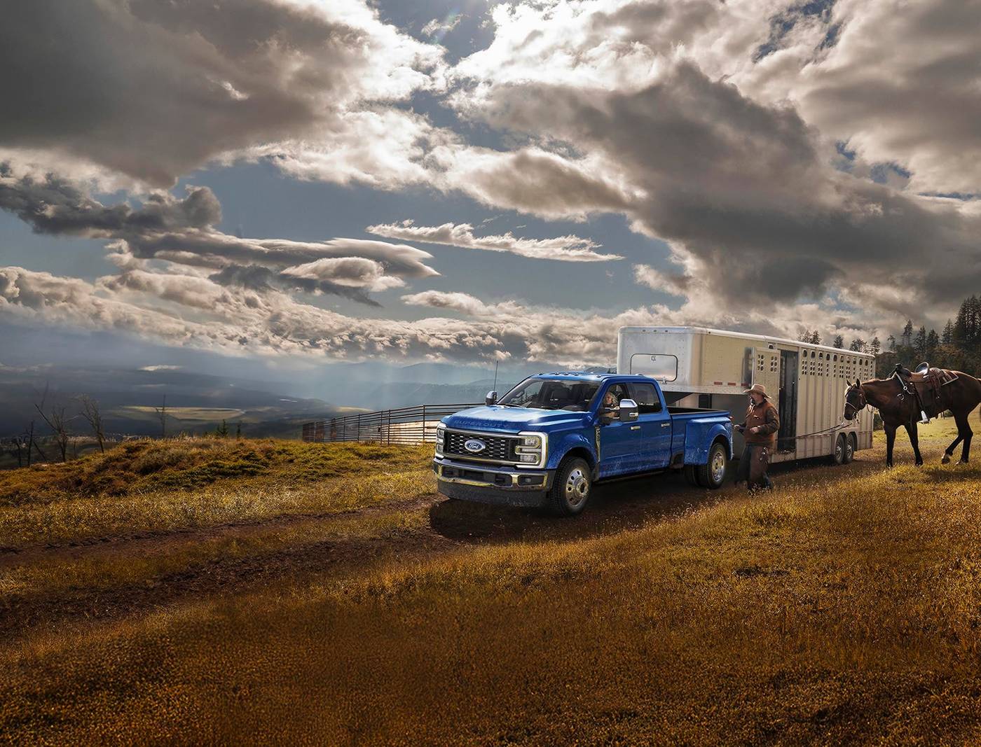 Blue Ford Super Duty crew cab hitched to a horse trailer in a pasture as a rider leads horses, Farmington MO
