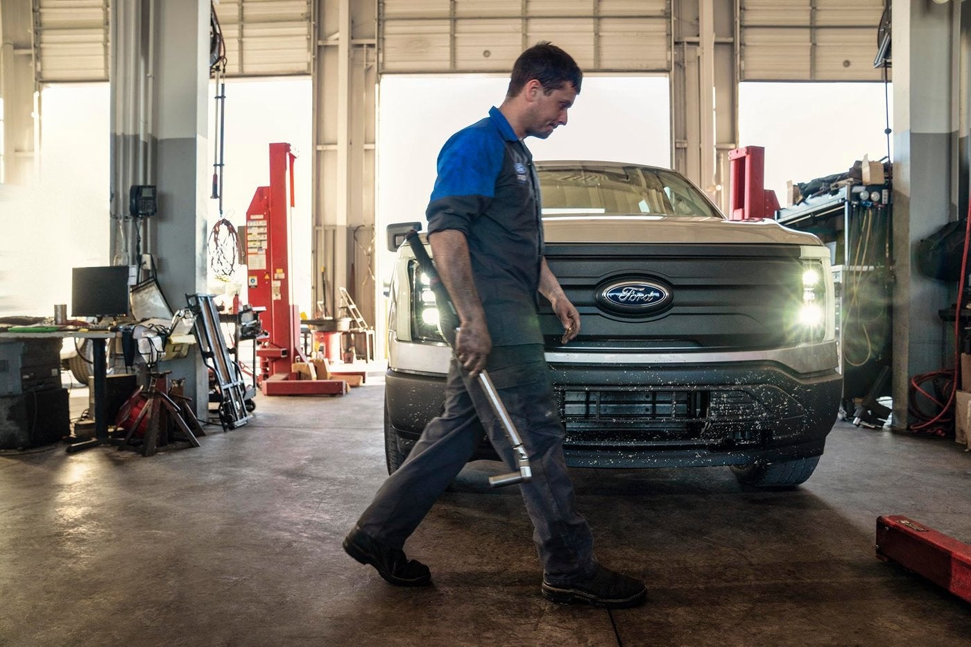 Ford technician walking through the service bay past a white Ford F-150 Lightning, AC checks in Farmington MO
