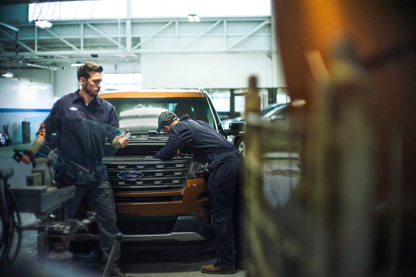 Two Ford technicians fitting front end parts on an orange Ford Explorer in the shop, genuine parts work in Farmington MO