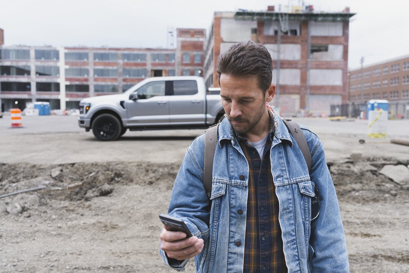 Man checking his phone at a job site with a silver Ford F-150 behind him, trade value research in Farmington MO