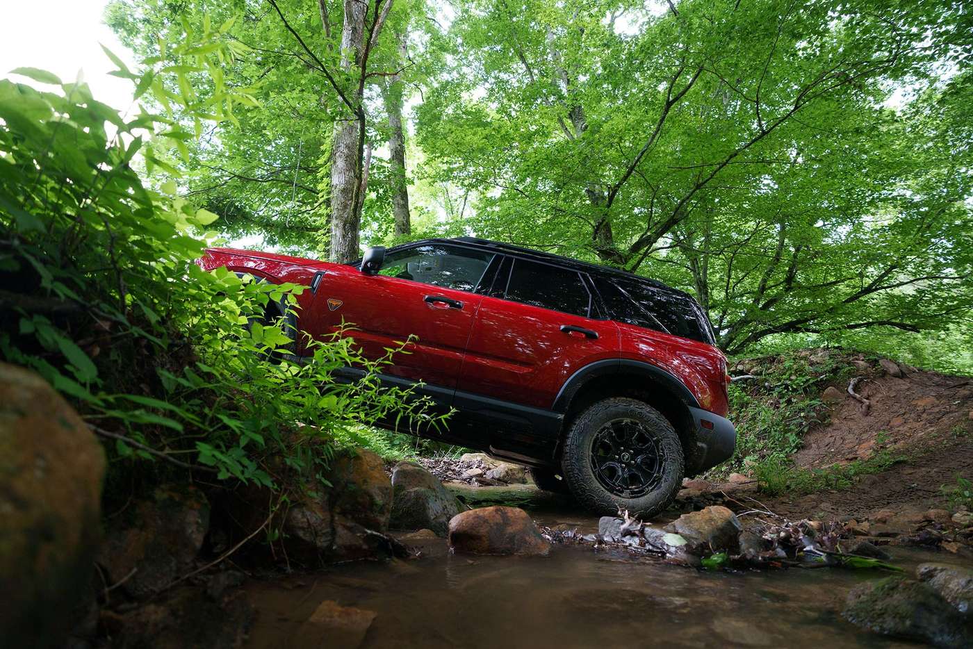 Red Ford Bronco Sport climbing rocks beside a creek in the woods, Farmington MO