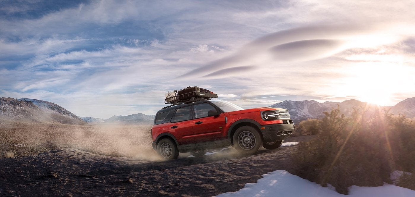 Red Ford Bronco Sport with roof gear climbing a snowy hillside trail, cold weather battery season in Farmington MO