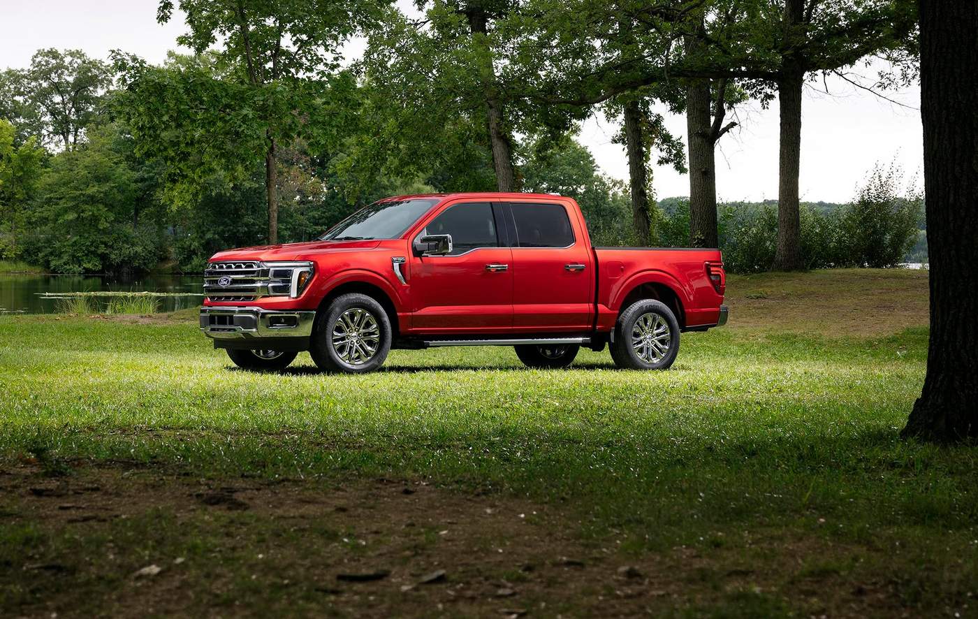 Red Ford F-150 Lariat SuperCrew parked on grass beneath shade trees by a lake, Farmington MO