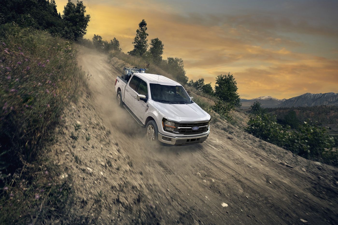 White Ford F-150 with an ATV in the bed kicking up dust on a gravel hill road, Farmington MO