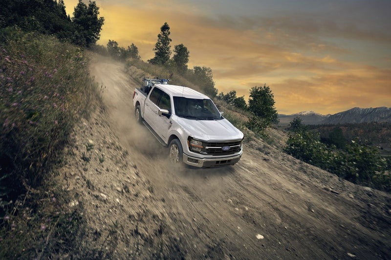 White Ford F-150 driving up a gravel hill road at sunset