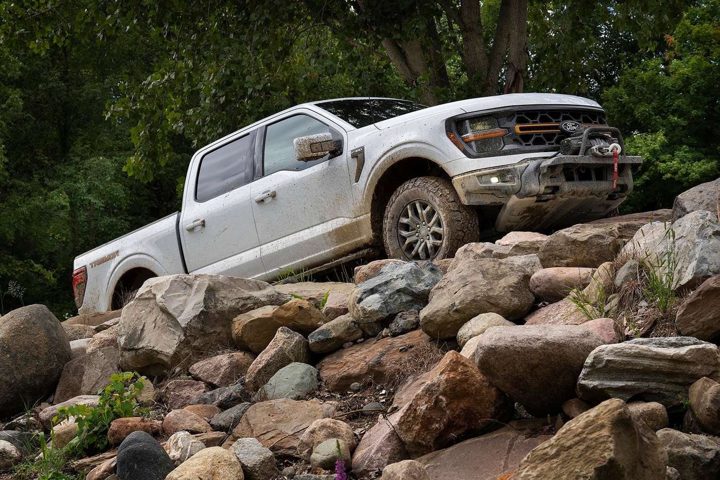 White Ford F-150 Tremor climbing a rocky slope in the woods, an off road F-150 trim for Farmington MO buyers