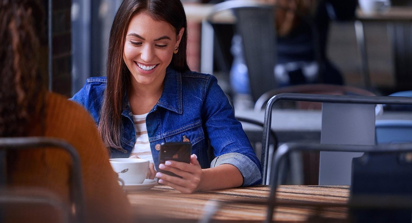 Smiling woman checking her phone at a cafe table Smiling woman checking her phone at a cafe table, a quick Ford recall lookup from Farmington MO