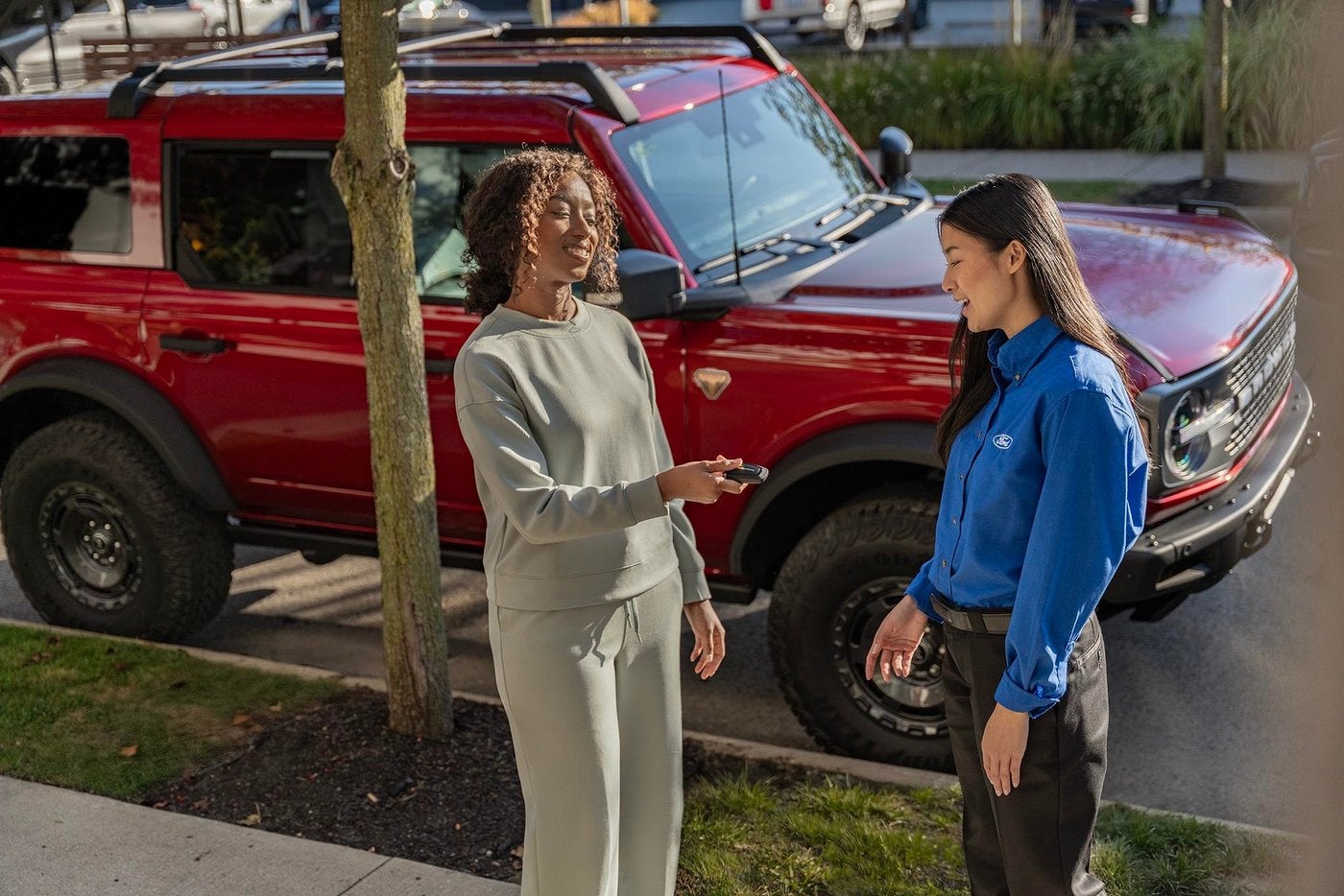 Woman handing a key fob to a Ford rep beside a red Ford Bronco at the curb, Farmington MO