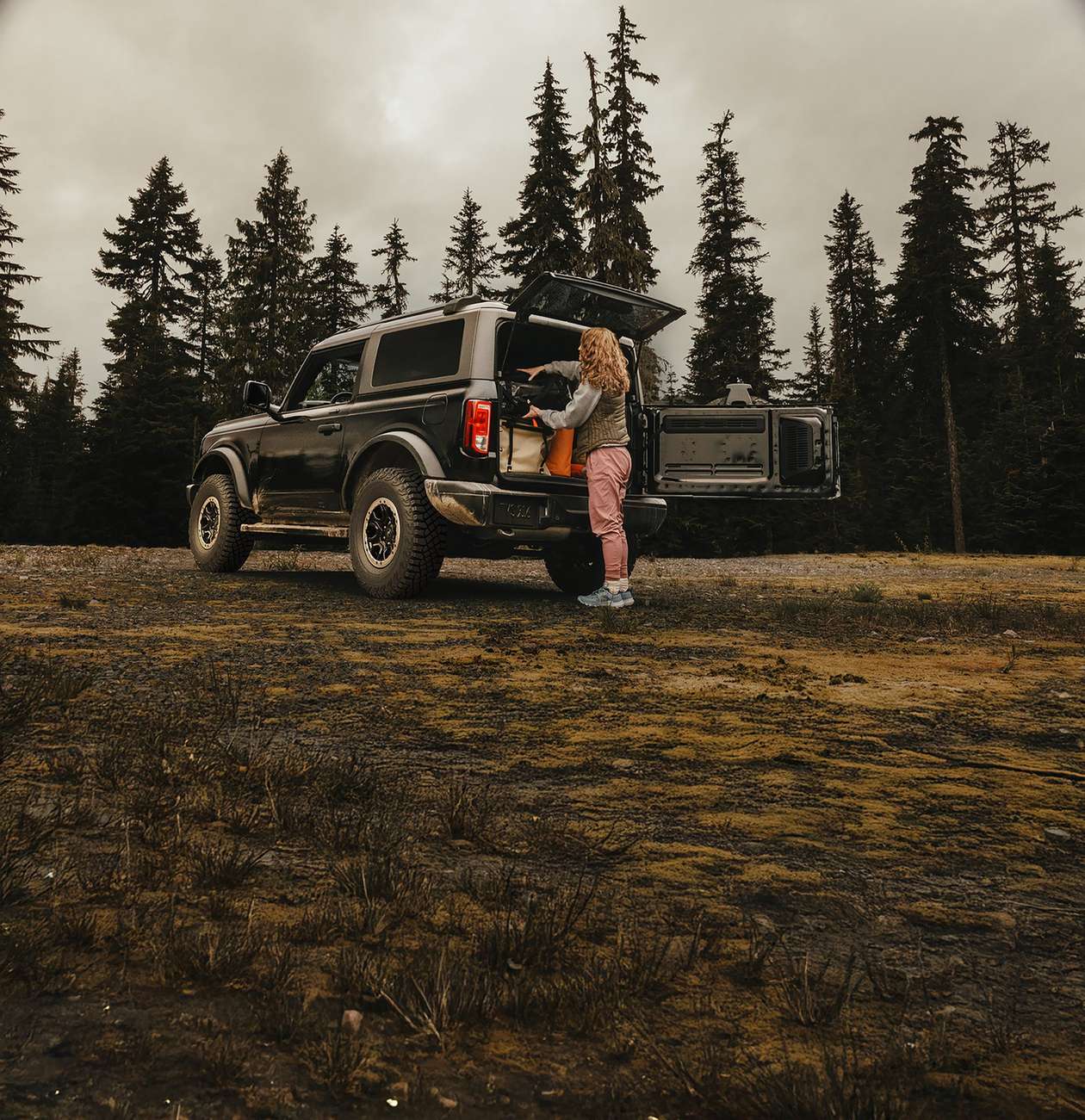 Woman unloading gear from the open tailgate of a Ford Bronco in a forest clearing Woman unloading gear from the open tailgate of a Ford Bronco in a forest clearing, Farmington MO